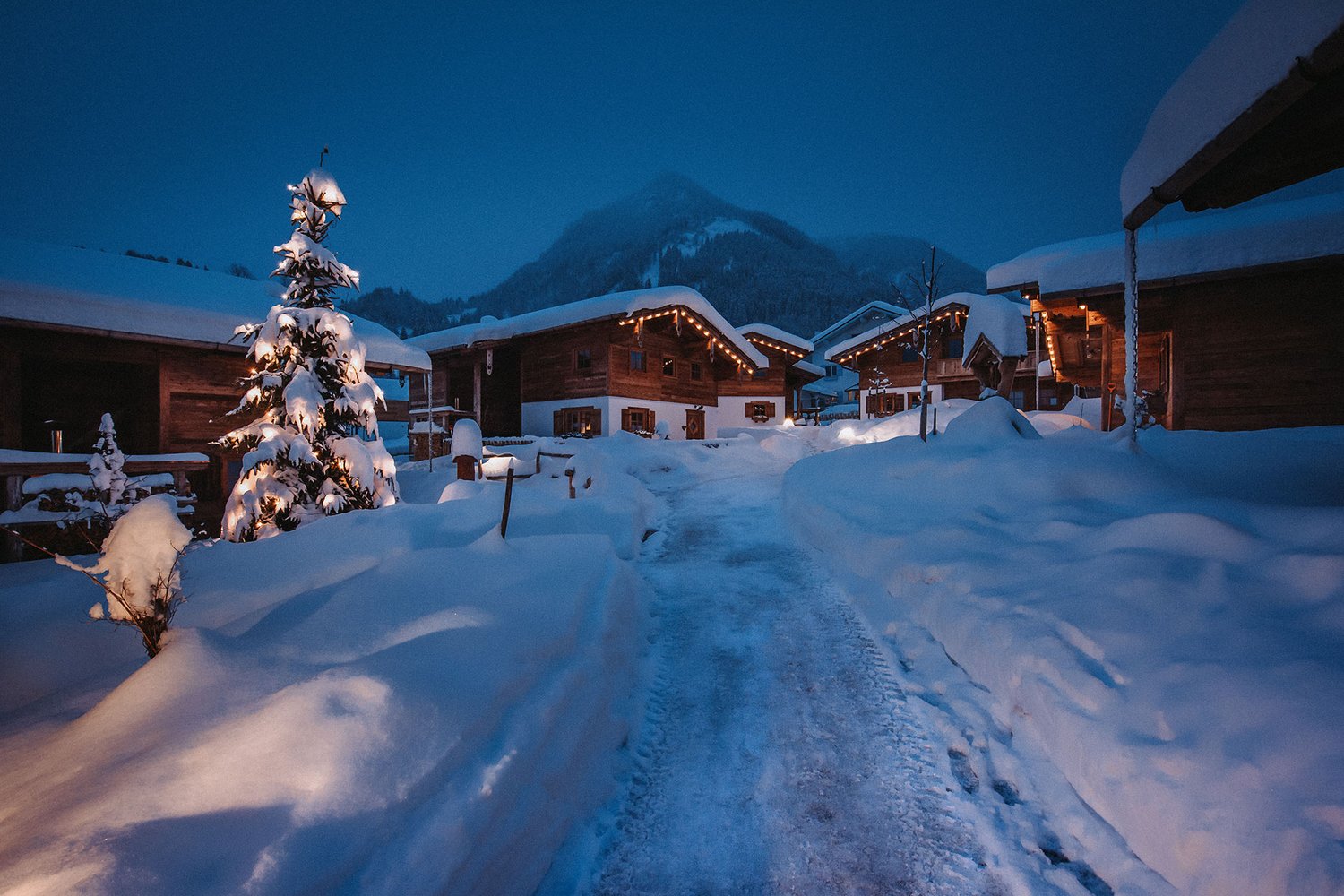 Ansicht des winterlich verschneiten Chaletdorfs am Abend mit weihnachtlicher Beleuchtung