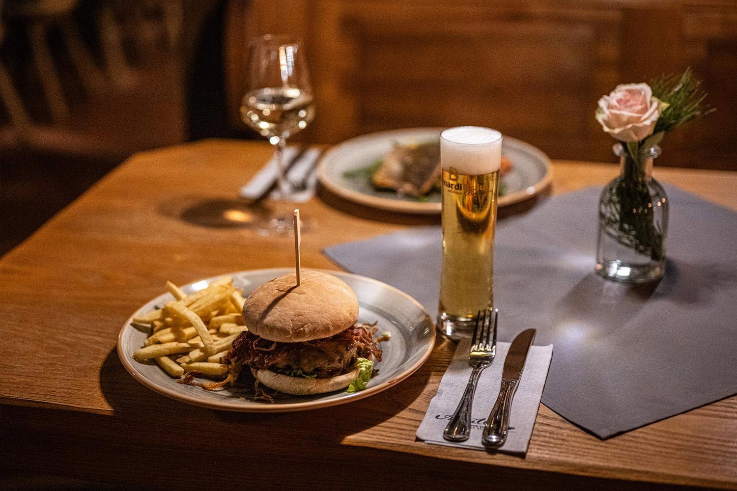 Bild eines Burgers mit Pommes und Bier auf einem eingedeckten Tisch