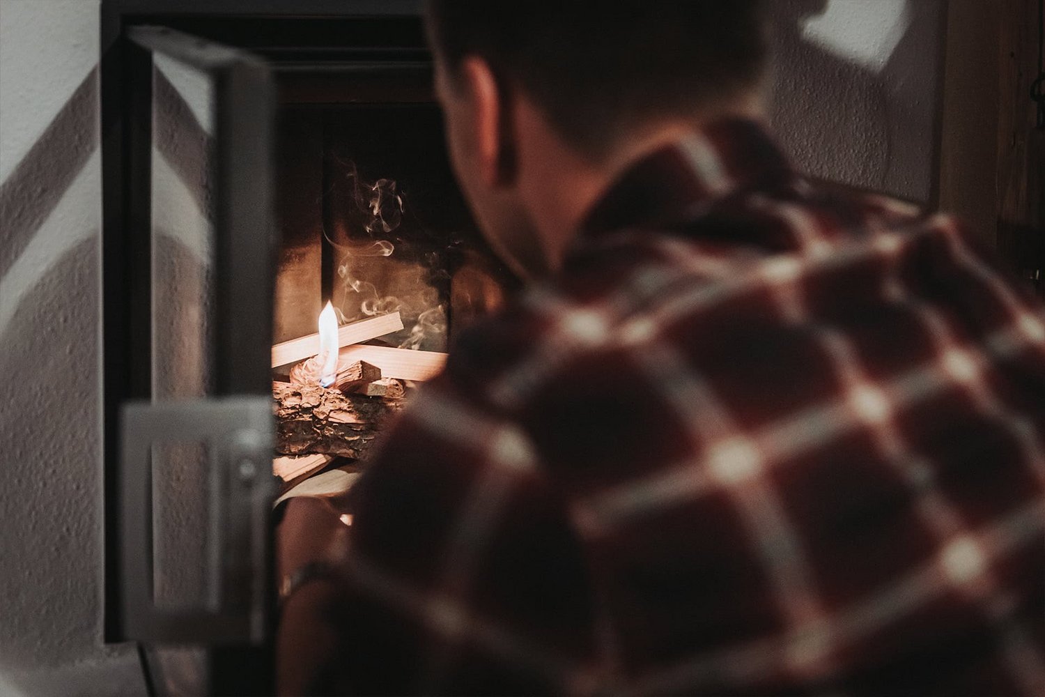 Ein Mann in karriertem Hemd entzündet ein Feuer im Kachelofen des Chalets