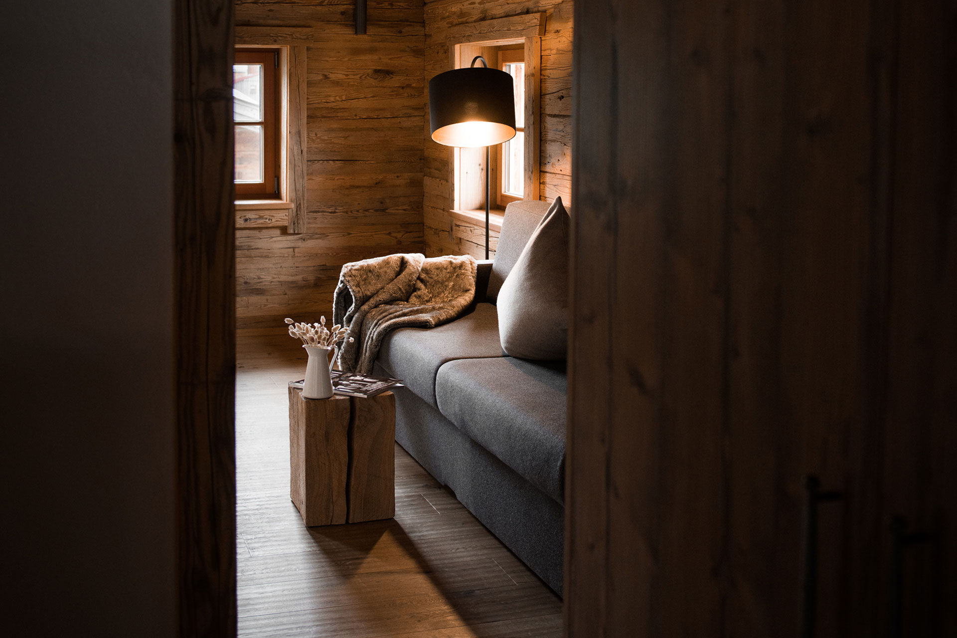 Einblicke in gemütliches Couchdetail eines Chalets mit Hocker, Blumen, Sofa und Leuchte
