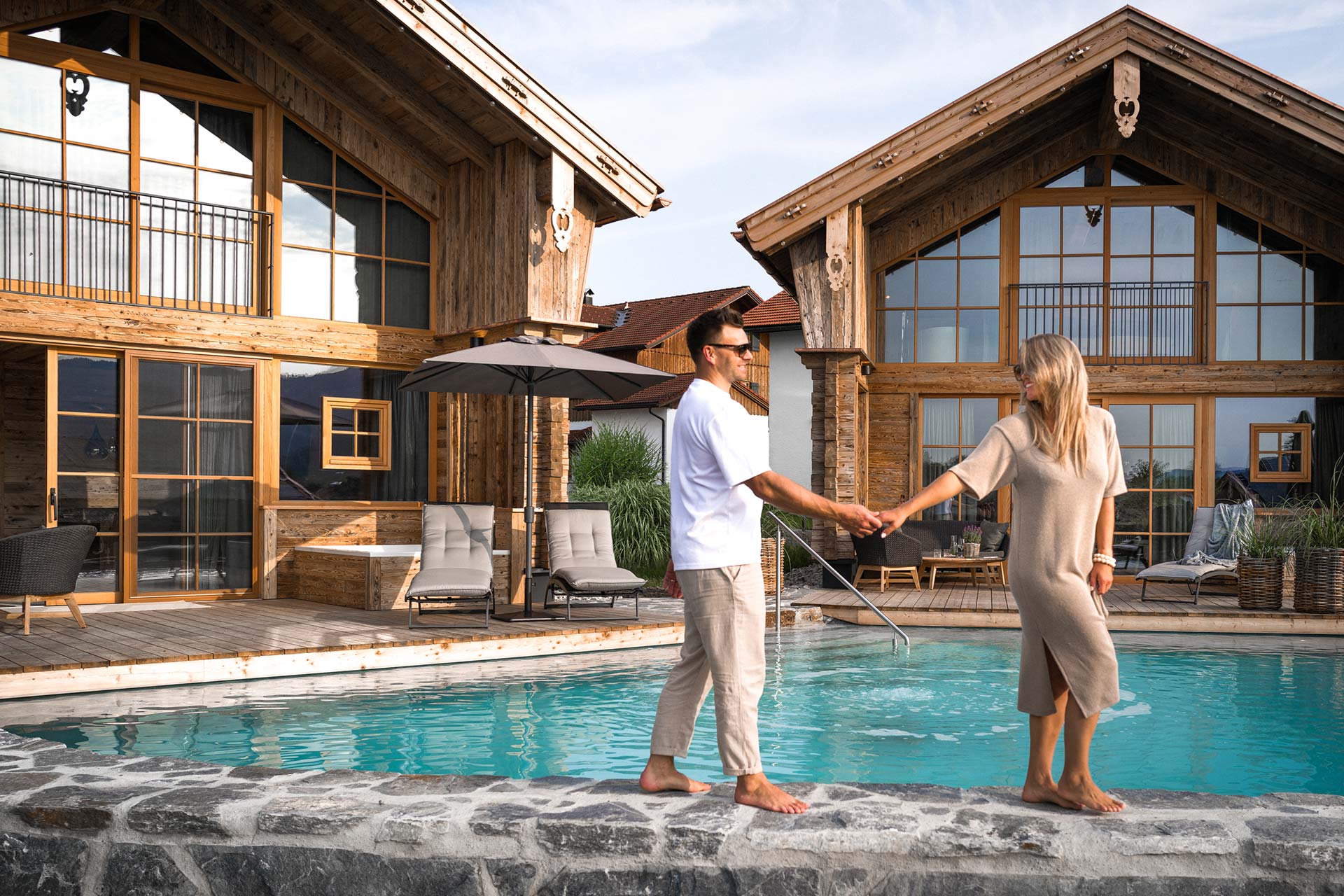 Paar händchenhaltend vor den beiden Premium Plus Chalets und dem privaten Naturbadesee