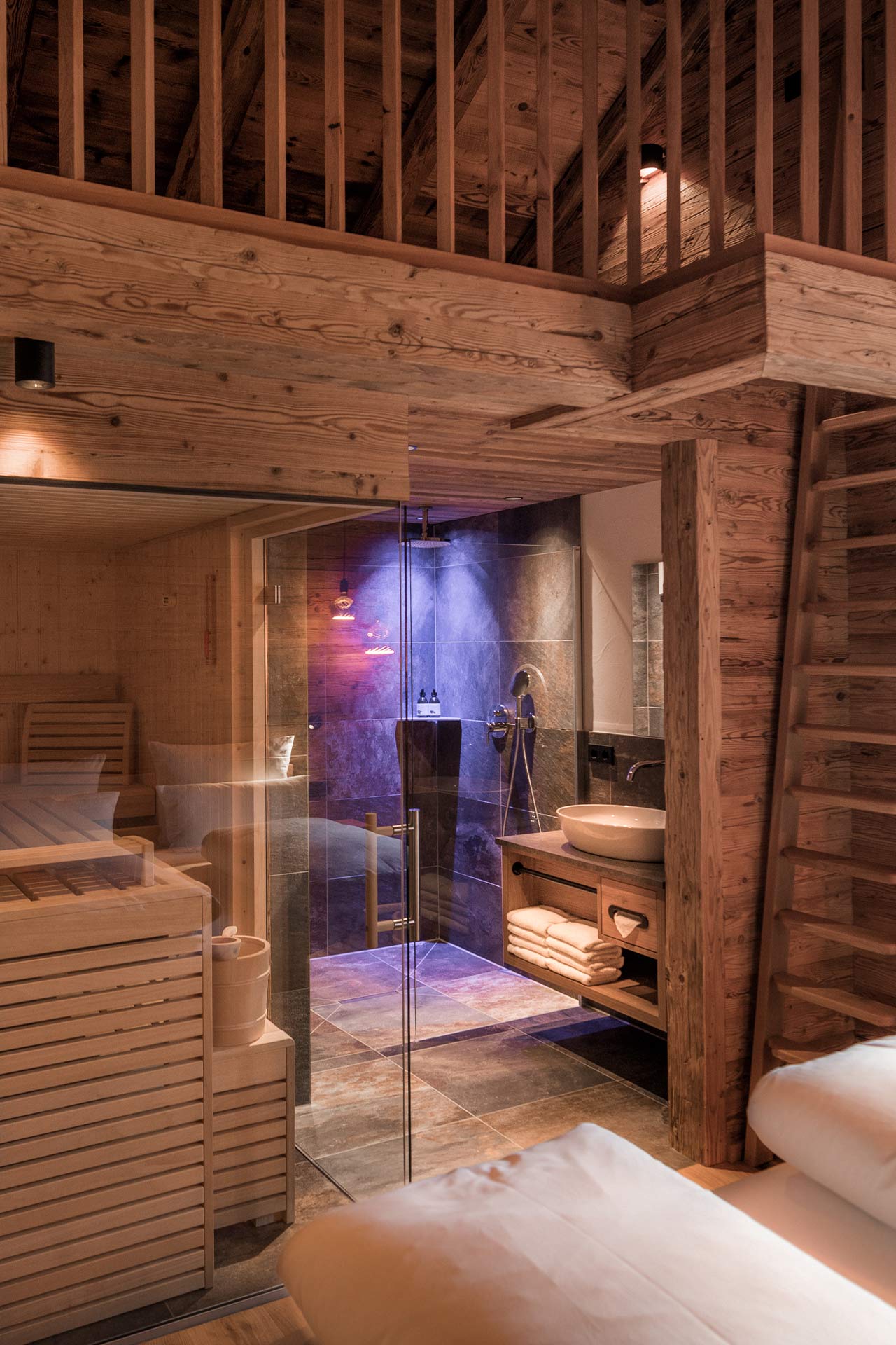 Ein modernes Spa mit Holzdetails und einer Glasdusche. Auf der linken Seite befindet sich eine Sauna, auf der rechten Seite ein Waschbereich mit einer modernen Armatur. Sanftes Licht und warme Farben schaffen eine entspannende Atmosphäre.