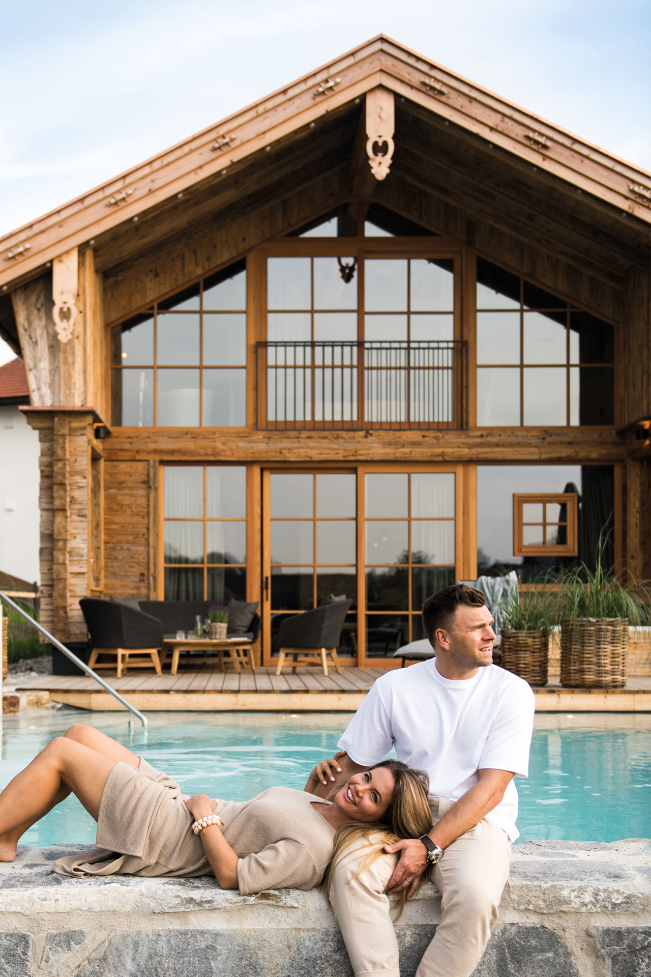 Paar lehnt sich gegenseitig vor Naturbadesee an, im Hintergrund Premium Plus Chalet