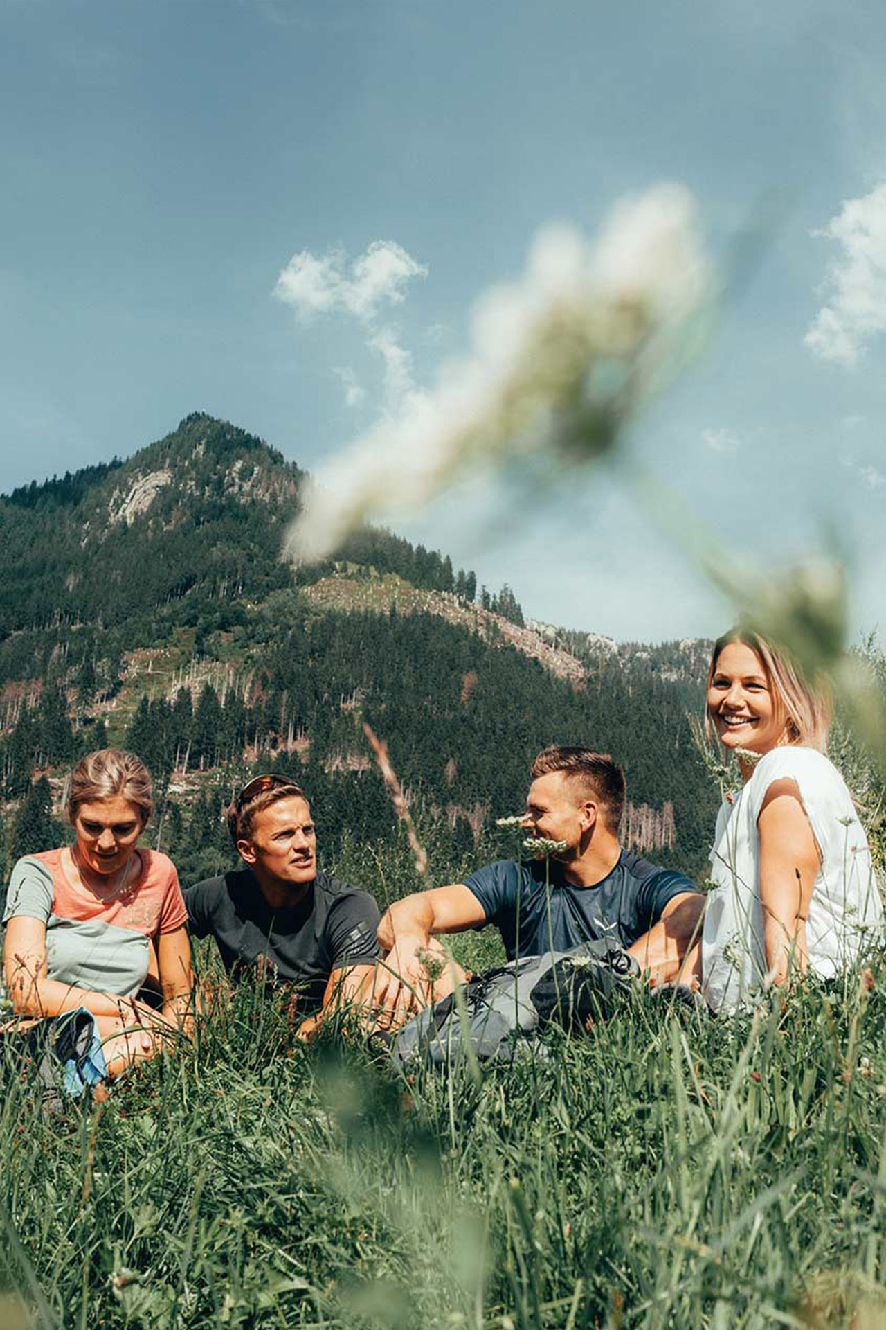 Zwei Paar sitzen im hohen Gras und machen eine Pause. Im Hintergrund ist das Burgberger Hörnle zu sehen