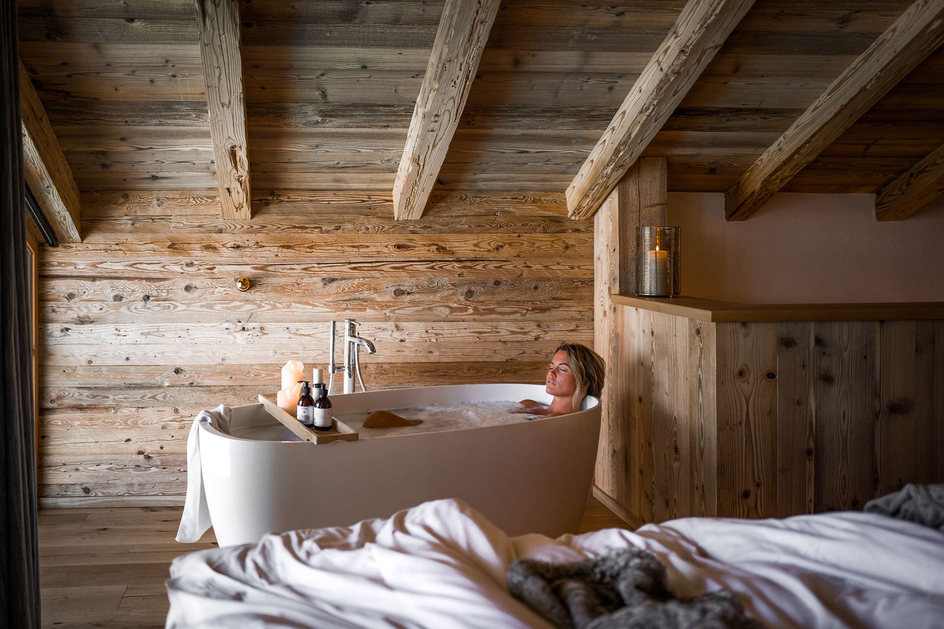 eine junge Frau genießt ein Bad in der freistehenden Badewanne ihres Chalets