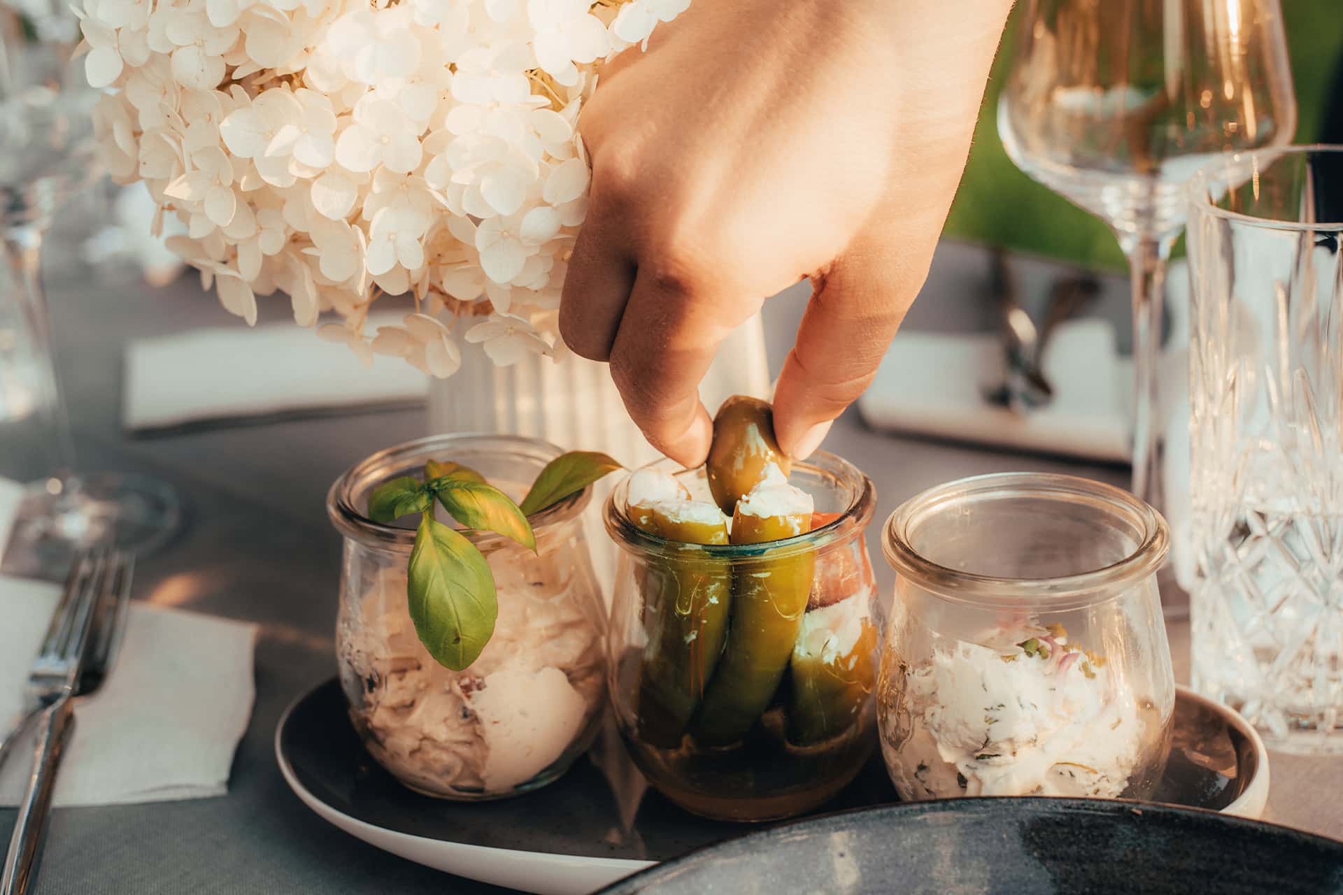 Eine hand bedient sich an frischer Antipasti auf einem sommerlich gedeckten Tisch