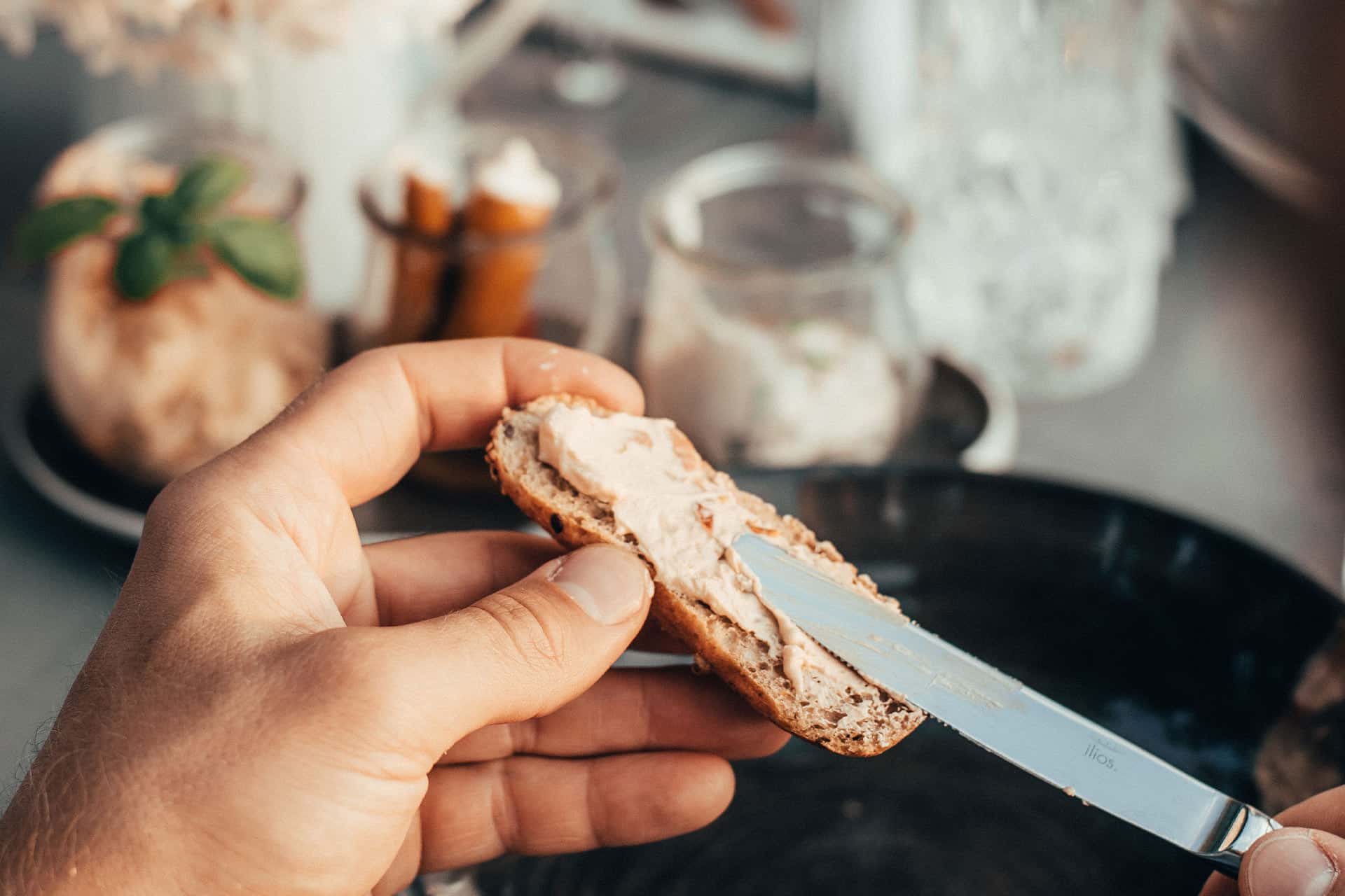 Detailaufnahme eines sommerlich gedeckten Tisches und einer Scheibe Brot mit frischem Aufstrich