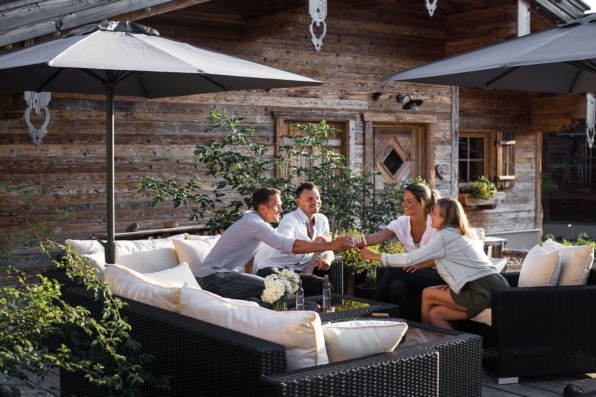 Zwei Paare sitzen in der Alpzitt Lounge und stoßen in der Abendsonne mit kühlen Getränken an