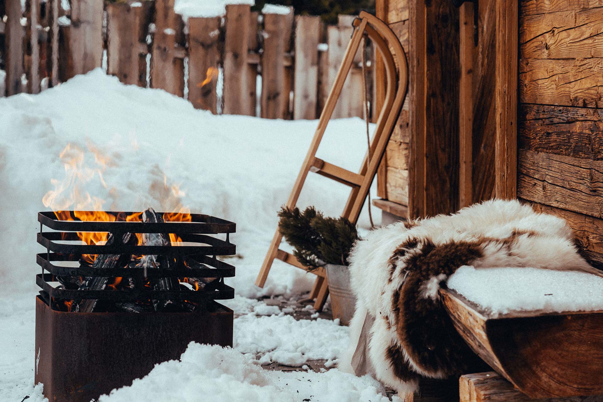 Detailaufnahme einer Feuerschale vor einem winterlich verschneiten Chalet