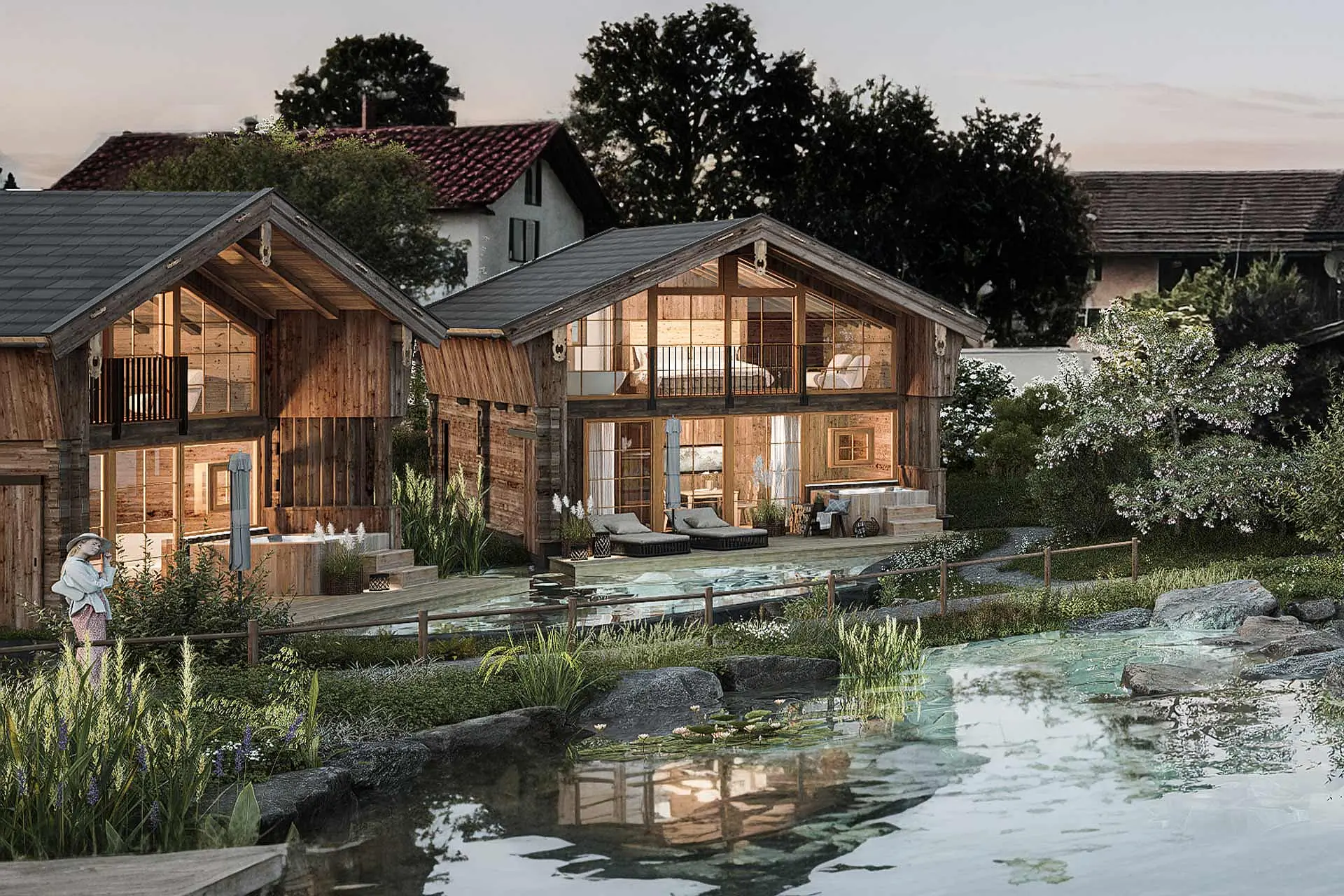 Two modern wooden houses are surrounded by greenery and a tranquil pond. The buildings feature large windows showing cozy interiors. Soft lighting from within the houses creates a warm and inviting atmosphere, while a person stands nearby, enjoying the serene landscape.
